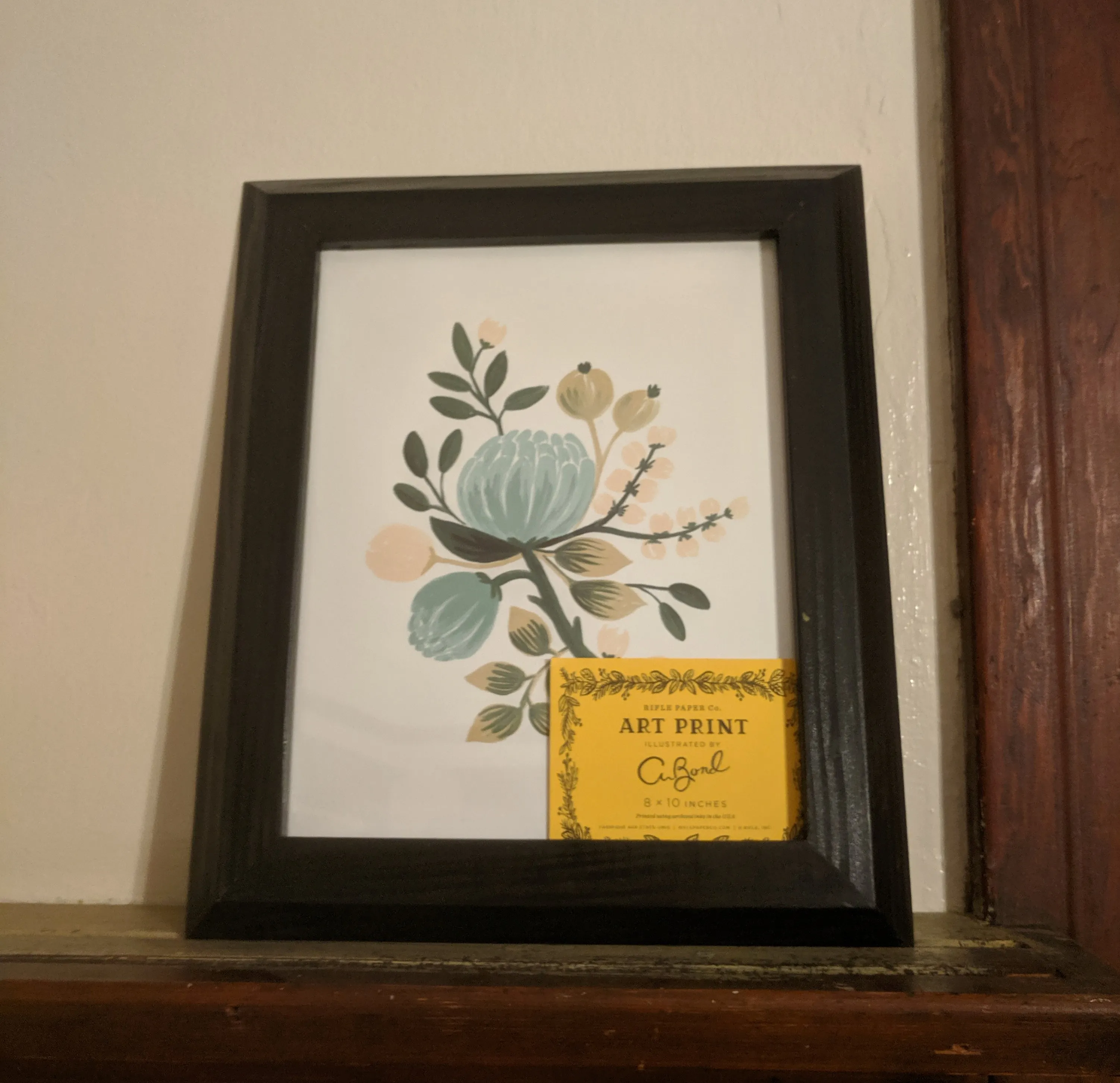 The frame sitting on a shelf containing the artwork